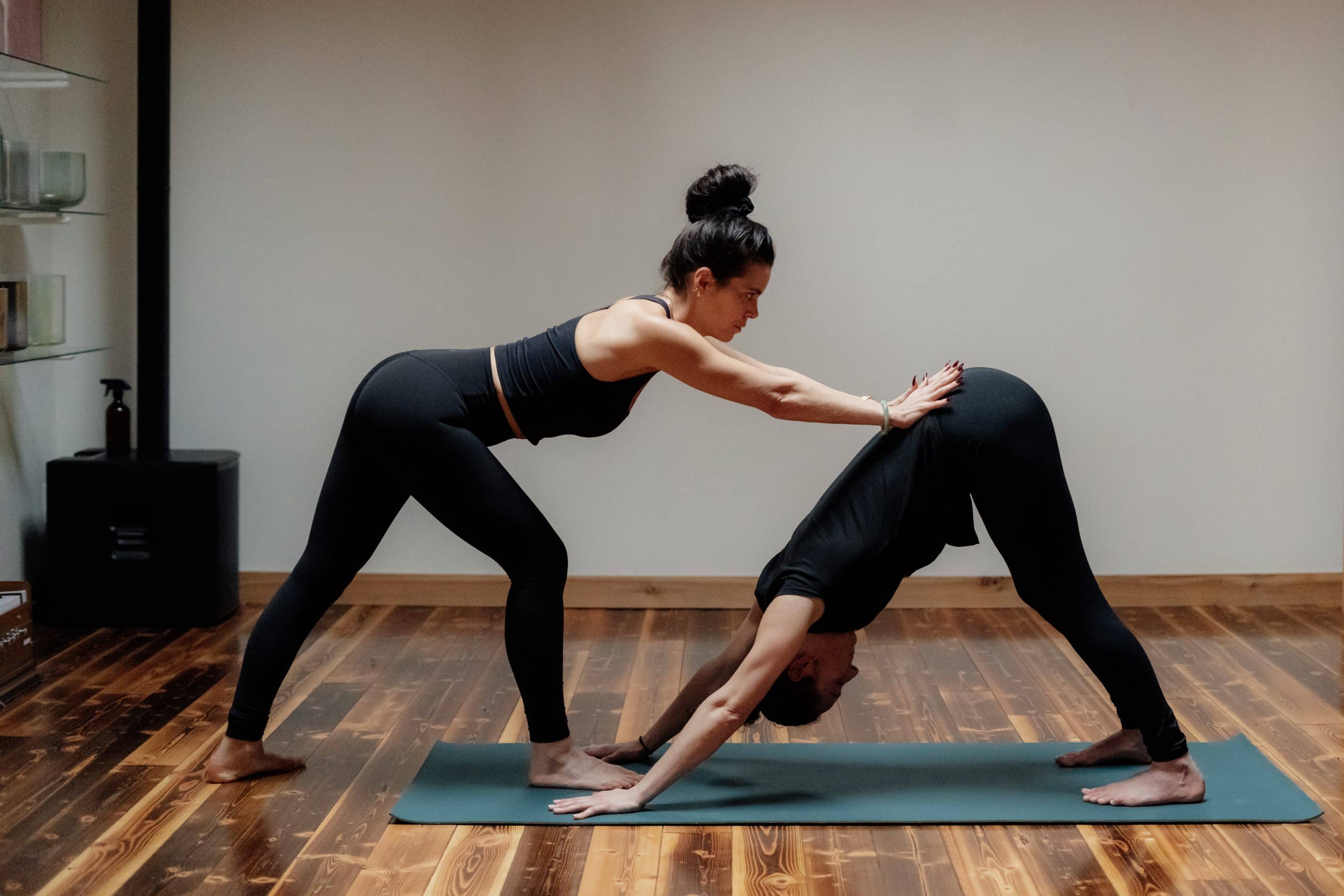 Woman instructor giving adjustment in Downward Dog pose