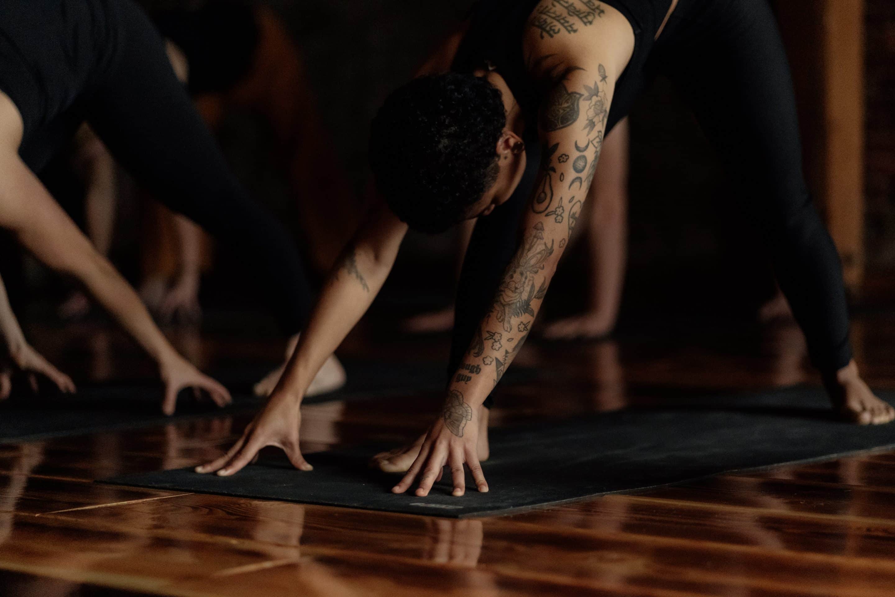 A woman with tattoos doing the Downward Dog pose during yoga practice.