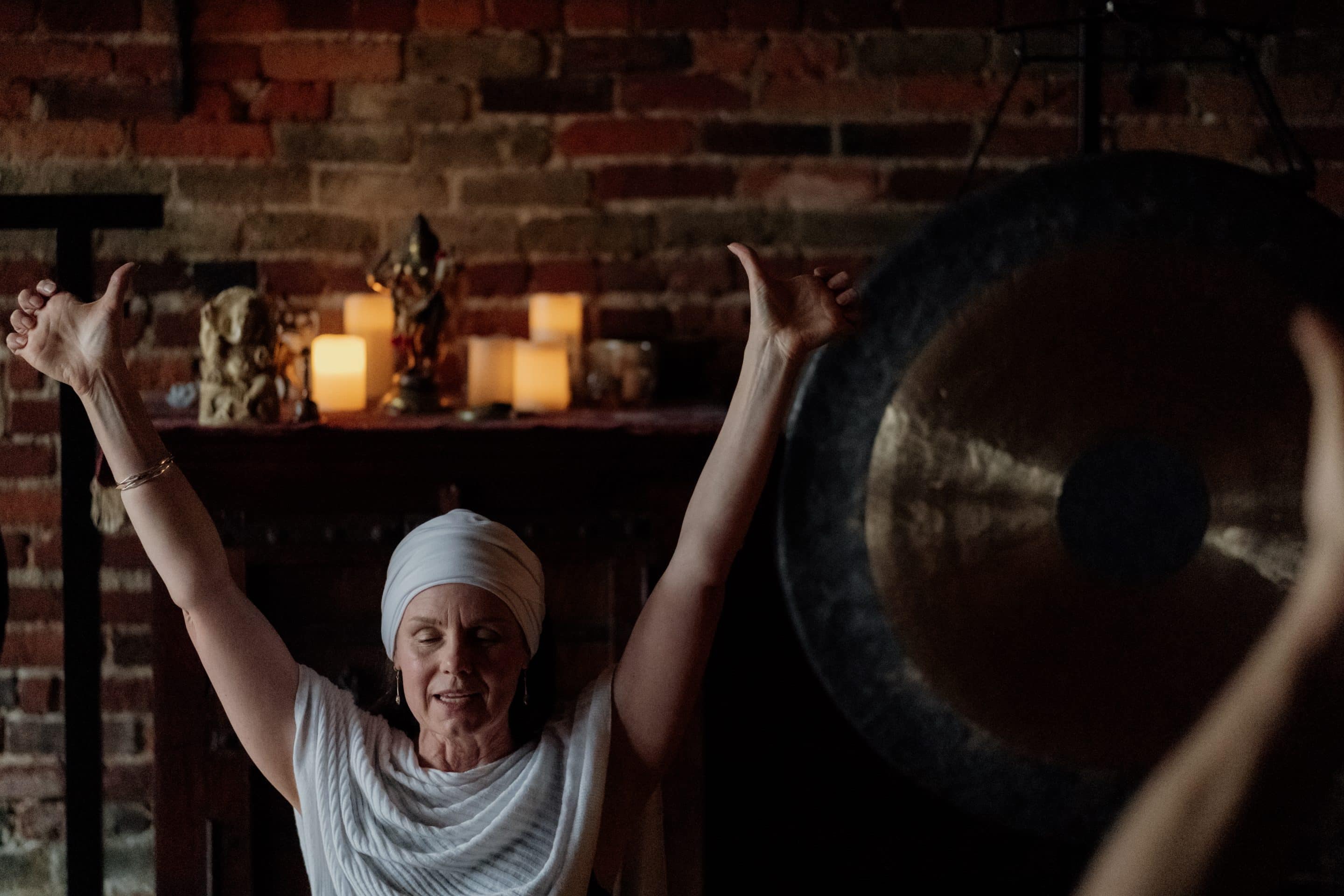 A woman wearing a turban practices yoga in a brick-walled room near a large gong.